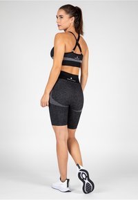Crni atletičarski set s sportskim grudnjakom s racerback i visokim kratkim hlačama. Materijal izgleda elastično s suptilnom teksturom i sivim naglascima.
