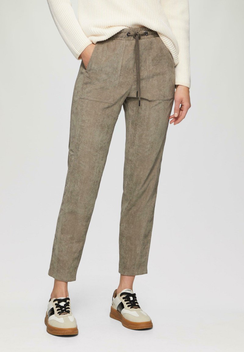 Lichtbruine stoffen broek met een zachte textuur, voorzien van een trekkoord in de taille en voorzakken, gecombineerd met zwart-witte sneakers.