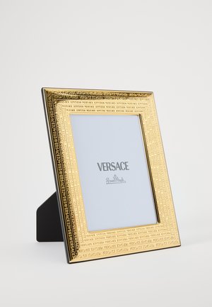 Zlatni metalni okvir za fotografije s utisnutim Versace logotipom, s crnom pozadinom. Područje za prikaz fotografije je pravokutno i prozirno.