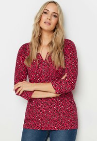 Blusa fucsia a maniche lunghe con motivo leopardato, dotata di scollatura a V con bottoni e vestibilità comoda. Tessuto morbido con leggero elastico.