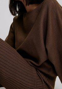 Brunstickad tröja med ribbad halsringning och ax seams, tillsammans med ribbade bruna leggings, båda med en mjuk textur.