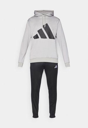 Felpa grigia con un grande logo triangolare nero e pantaloni della tuta neri coordinati con un piccolo logo. Tessuto morbido con polsini a costine.