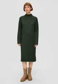 Długo-słowowa sukienka w ciemnozielonym kolorze z wysokim kołnierzem, bocznymi rozcięciami i luźnym krojem; zestawiona z jasnobrązowymi botkami za kostkę z elastycznym bokiem.