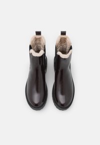 Brown leather ankle boots with a smooth finish, shearling trim at the top, and a black rubber sole. Features a pull tab for easy wear.