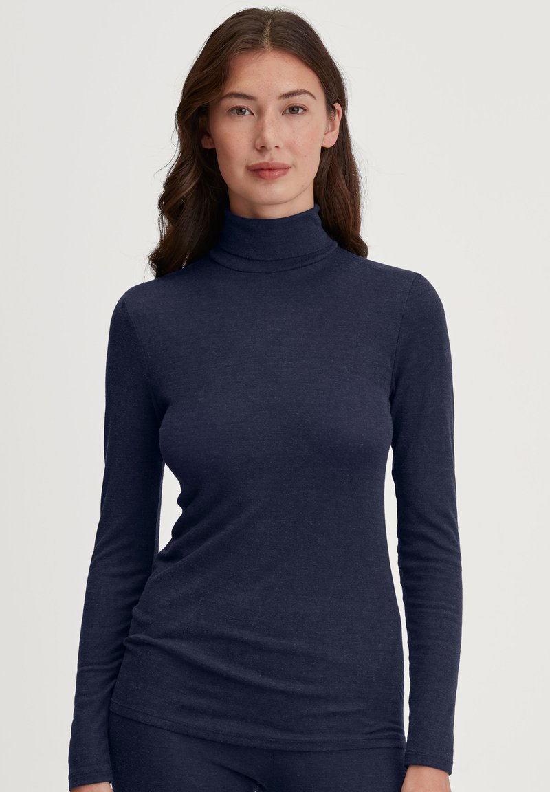 Marineblauwe coltrui gemaakt van een zachte, lichte stof. Heeft lange mouwen en een aansluitende silhouet met een zachte textuur.