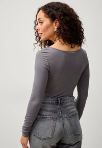 Langärmliges graues Oberteil mit rundem Halsausschnitt und tailliertem Design, kombiniert mit hochsandigen, ausgewaschenen schwarzen Jeans mit Gesäßtaschen.