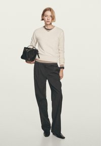 Kremowy sweter w serek, ciemne eleganckie spodnie, czarna torebka, gładka faktura. Sweter ma kontrastowy dolny brzeg i miękkie wykończenie.