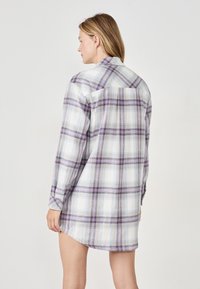 Koszula z długim rękawem w kratę w kolorze białym, purpurowym i niebieskim. Posiada guziki, kołnierzyk oraz zaokrąglony dół. Widok z tyłu eksponuje szew yoke.