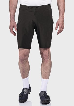 Schwarze Shorts aus leichtem Material mit flachem Bund, zwei Knöpfen und Seitentaschen. Getragen mit weißen Socken und schwarzen Radschuhen.