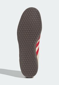 Sneakersula i brunt gummi, med ett hexagonalt mönster för grepp. Vit, beige och röd ovandel med tre röda ränder på sidan.