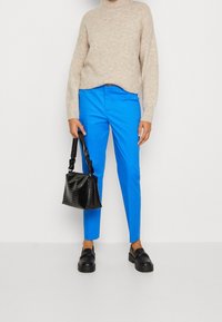 Niebieskie dopasowane spodnie, beżowy dzianinowy sweter, czarna torebka o fakturowanej powierzchni z twistsanym uchwytem oraz czarne buty wsuwane na grubej podeszwie.