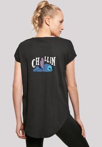 Camiseta negra de manga corta con dobladillo redondeado. Presenta el texto "CHILLIN" y un personaje de dibujos animados azul tumbado en la espalda.