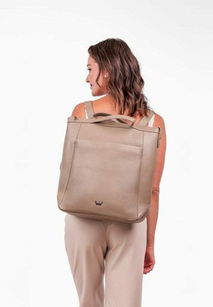 Beige kožený batoh s hladkým povrchem, vybavený dvojicí horních uší a přední kapsou, vystavený na modelu zádní stranou.
