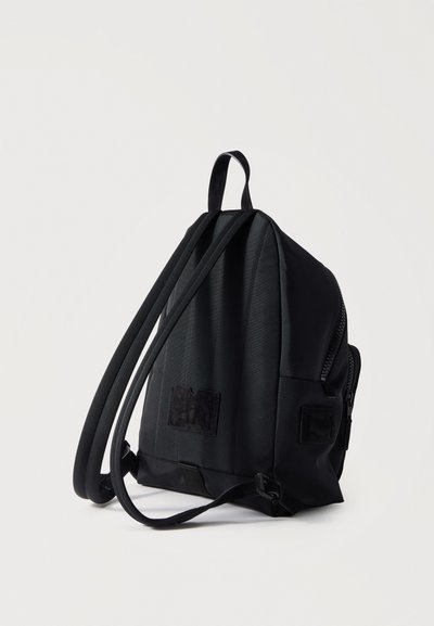 Μαύρο συμπαγές σακίδιο με δύο ρυθμιζόμενους ιμάντες ώμου και κλείσιμο με φερμουάρ, τοποθετημένο όρθιο σε απλό φωτεινό φόντο.