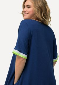 Navy blauwe top met korte mouwen en een losse pasvorm, voorzien van een textuurstof en kleurrijke groene en witte gestreepte accenten op de manchetten.