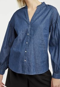 Denimskjorta med knappar, v-ringad, långa ballongärmar och en volangkrage. Fastsydd med silverfärgade knappar fram.