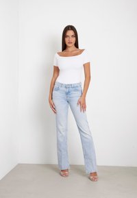Bodysuit blanco ajustado y sin mangas combinado con jeans acampanados de color azul claro. La modelo está en un entorno neutral y sin adornos.