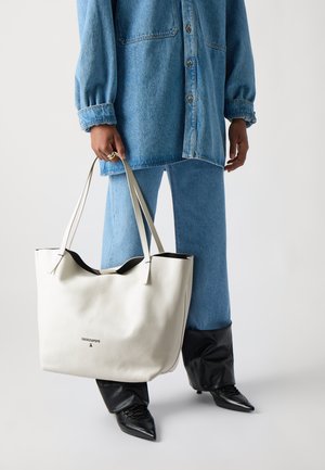 Borsa tote in pelle bianca con interno nero, dotata di due manici lunghi e un logo sottile sul davanti. Modella che indossa un outfit in denim.