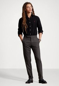 Sort knappeskjorte med lange ermer, grå teksturerte bukser med rett snitt, og svarte lærsko. Enkel klokke som tilbehør.