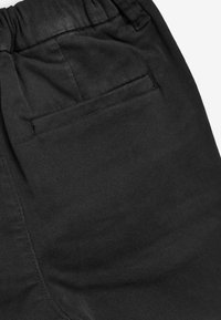 Pantalons en denim noir avec une taille élastique, dotés d'une poche arrière et d'une texture lisse. Des coutures minimales sont visibles.