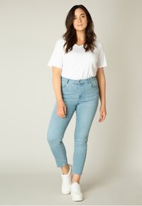 Lichtblauwe high-waisted jeans met rafelige zoom, gecombineerd met een witte V-hals t-shirt en witte sneakers. Smooth textuur, aansluitend ontwerp.