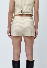 Beige stribede shorts med en skræddersyet pasform, der har høj talje, bæltestropper og en baglomme. Stoffet har en glat tekstur.