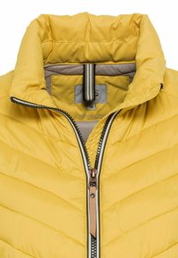 Veste matelassée jaune avec col haut, fermeture éclair rayée noire et blanche, et tirette beige, taille 36, fabriquée à partir de matériaux recyclés.