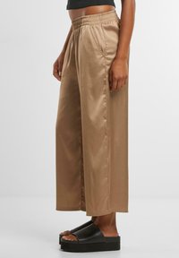 Beige satin wide-leg pants with an elastic waistband and side pockets, featuring a smooth texture and a loose, flowy silhouette.