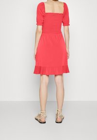 Rotes, knielanges Kleid mit einem gerafften Oberteil, quadratischem Ausschnitt und Puffärmeln. Hat einen ausgestellten Saum und wird mit Riemchensandalen kombiniert.