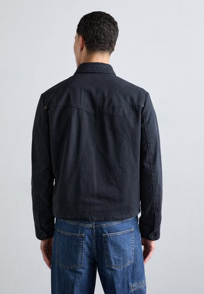 Black denim jacket with a collar, long sleeves, and back yoke detail. Paired with blue denim pants featuring visible back pockets.