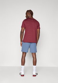 Korte mouw bordeauxrode textured shirt gecombineerd met lichtblauwe shorts, geaccentueerd met witte sneakers en sokken met een logo.