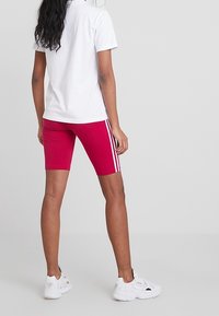 Röda cykelbyxor med vita sidostrecker, tillsammans med en vit polotröja. Byxorna är gjorda av ett elastiskt, andningsbart material.