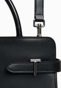 Borsa a tracolla in pelle nera con un mezzanino a forma di T in argento e tracolla rimovibile attaccata da un gancio in argento.