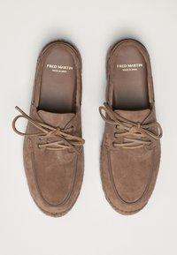 Brown suede loafers with a rounded toe, stitched detailing, and brown lace accents. "FRED MARTIN MADE IN SPAIN" printed inside.