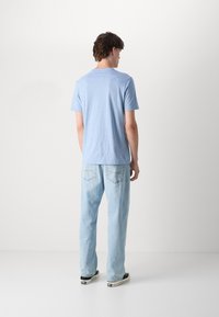 T-shirt de mangas curtas azul claro, feito de tecido suave, combinado com jeans de lavagem clara. Design simples, ajuste casual e decote redondo clássico.