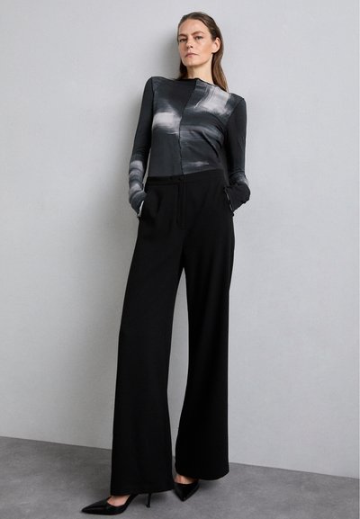 Black wide-leg trousers with a tailored waist. Fitted long-sleeve top featuring abstract grey and black patterns. Smooth fabric texture.