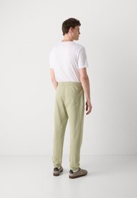 Hellgrüne, locker sitzende Jogginghosen mit elastischem Bund, gerippten Knöcheln und einer Gesäßtasche. Getragen mit einem schlichten weißen T-Shirt.