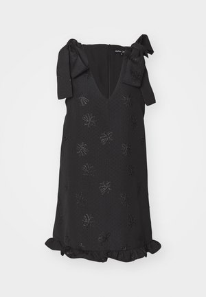 Black sleeveless dress featuring a V-neck, bow accents on shoulders, embossed floral pattern, and ruffled hem. Textured fabric adds depth.