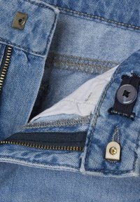 Tela de mezclilla azul clara con cremallera de latón y detalles en plata. Se puede ver un forro blanco en el área del bolsillo, con detalles de costura.