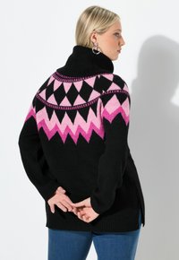 Maglione nero con colletto alto, caratterizzato da un motivo a zigzag rosa e nero. Tessuto a maglia, maniche lunghe e spacchi laterali all'orlo.
