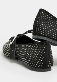 Bailarinas de ante negro con puntera puntiaguda, adornadas con tachuelas plateadas en un diseño, que cuentan con una correa con hebilla y una suela de goma plana.