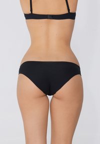 Bas de bikini noir avec une texture lisse, design taille basse et couverture minimale. Lignes simples et épurées sans motifs ni accents visibles.