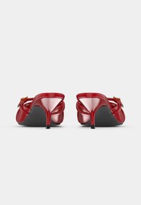 Červené lakované vysoké podpätky so zabudovanými remienkami, zobrazené zozadu na bielom pozadí.