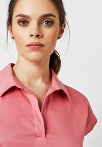 Rosa Poloshirt mit Kragen und kurzen Ärmeln, ausgestattet mit einer Knopfleiste und glattem Material. Der Stoff hat ein weiches Aussehen.