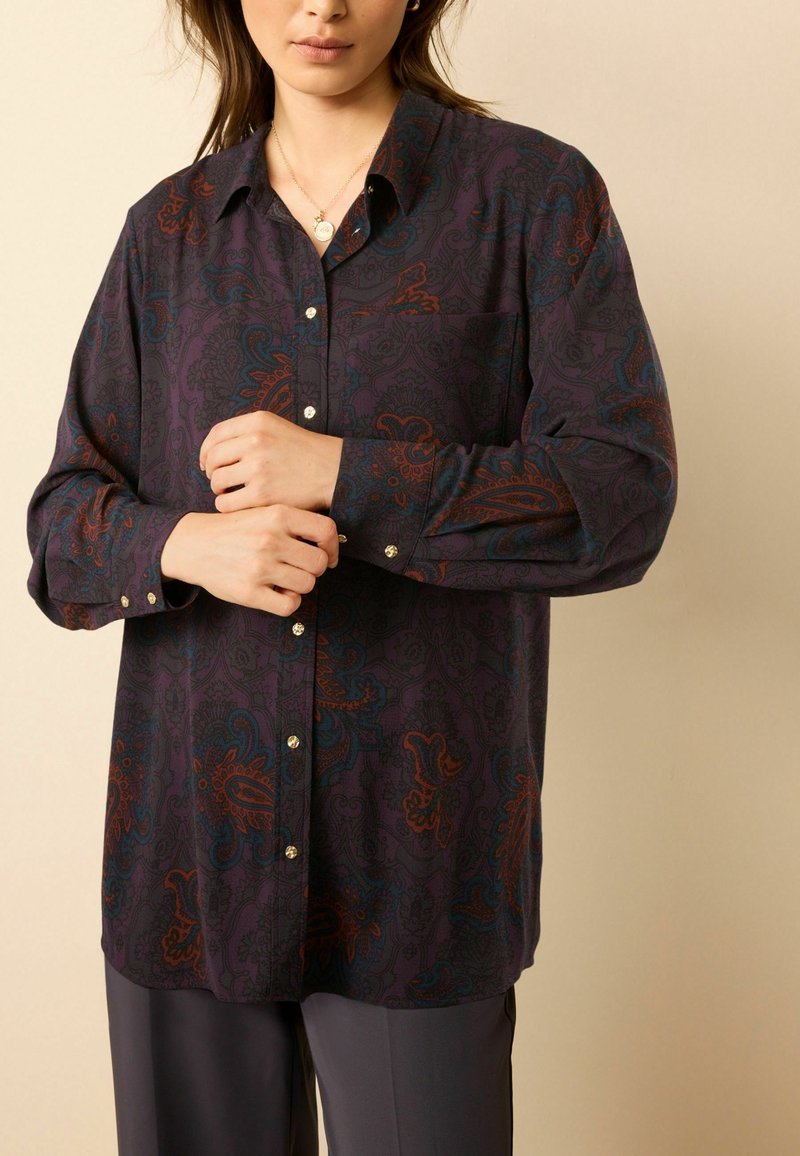Long-sleeve shirt in dark purple fabric, featuring an intricate paisley pattern in red and teal, with button-up front and collar details.