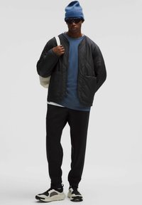 Fekete steppelt dzseki, kék hosszú ujjú póló, fekete nadrág, kék kötött sapka, fekete napszemüveg és fekete-fehér sportcipő. Állítható pántok a táskán.