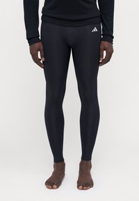 Schwarze Sportleggings aus dehnbarem Material, mit engem Design, elastischem Bündchen und einem kleinen weißen Logoakzent an der Seite.