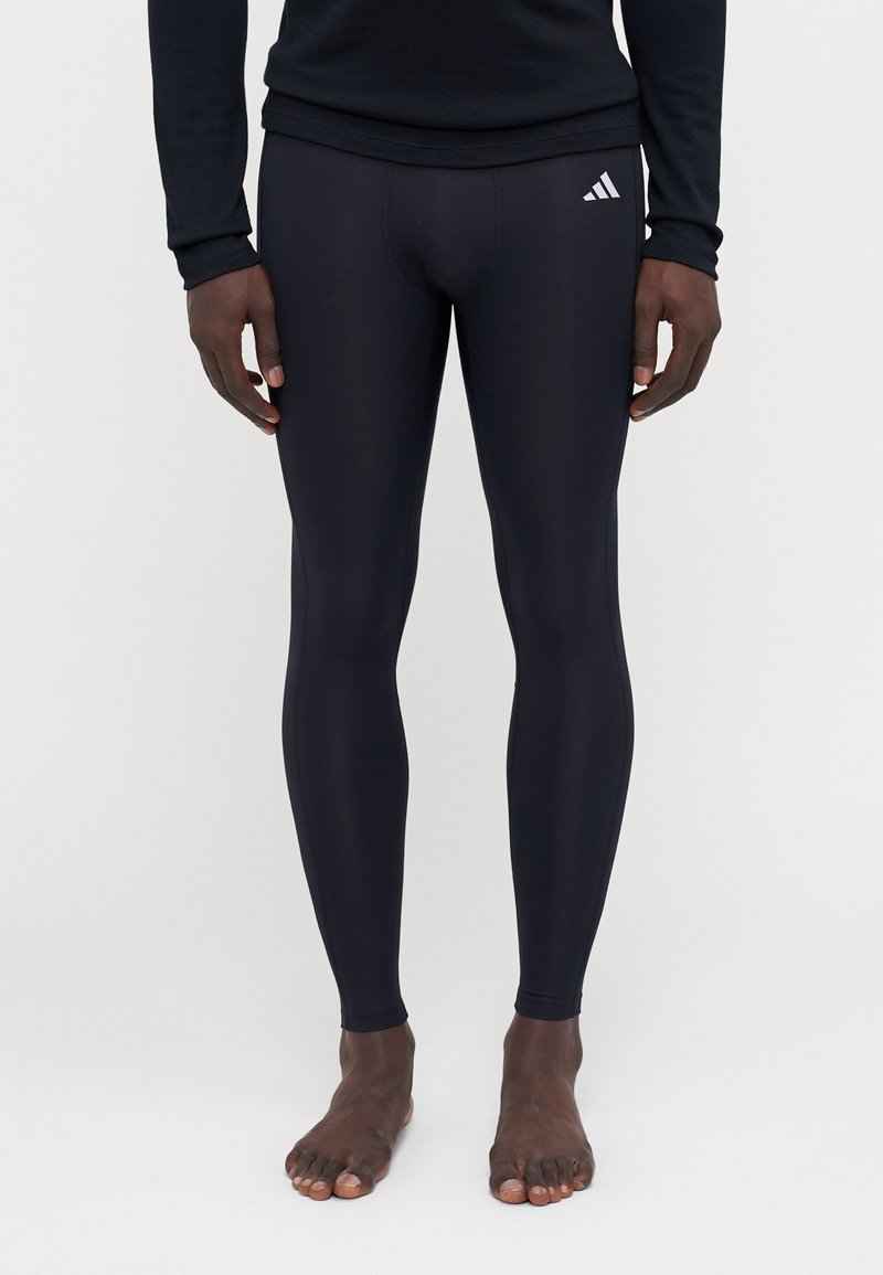 Schwarze Sportleggings aus dehnbarem Material, mit engem Design, elastischem Bündchen und einem kleinen weißen Logoakzent an der Seite.