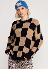 Chunky stickad tröja med ett rutmönster i beige och svart, med ribbad textur och en avslappnad passform. Kombineras med byxor i leopardmönster.