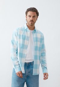Hellblau-weiß kariertes Hemd mit Knöpfen, langen Ärmeln, über einem weißen T-Shirt getragen, kombiniert mit hellblauen Jeans. Glatte Textur.